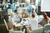 a group of people sitting at a meeting table with documents out having a discussion